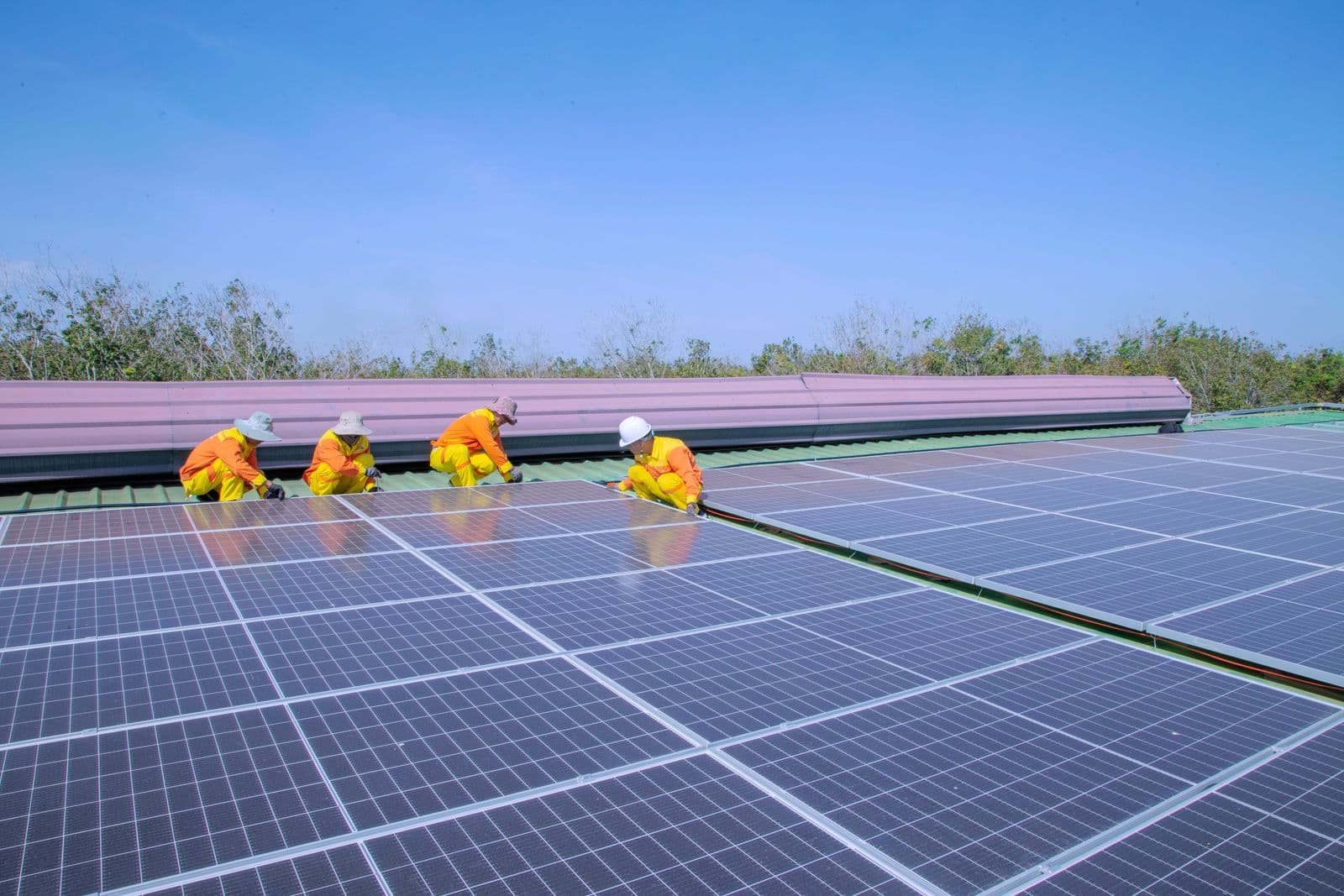 Two technicians installing solar panels on a roof on a clear day.