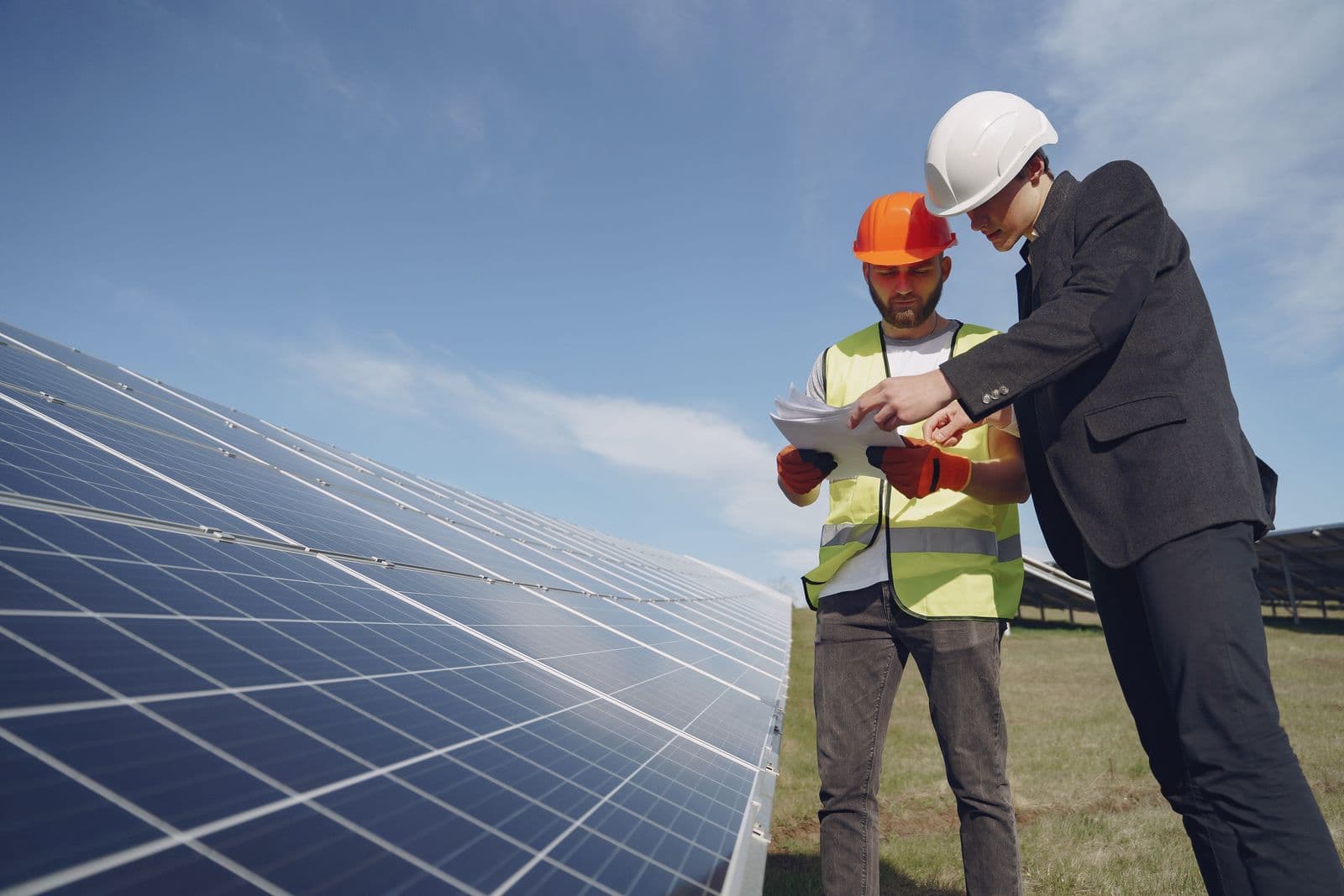 Two inspectors in hard hats checking documentation against an installed solar array.