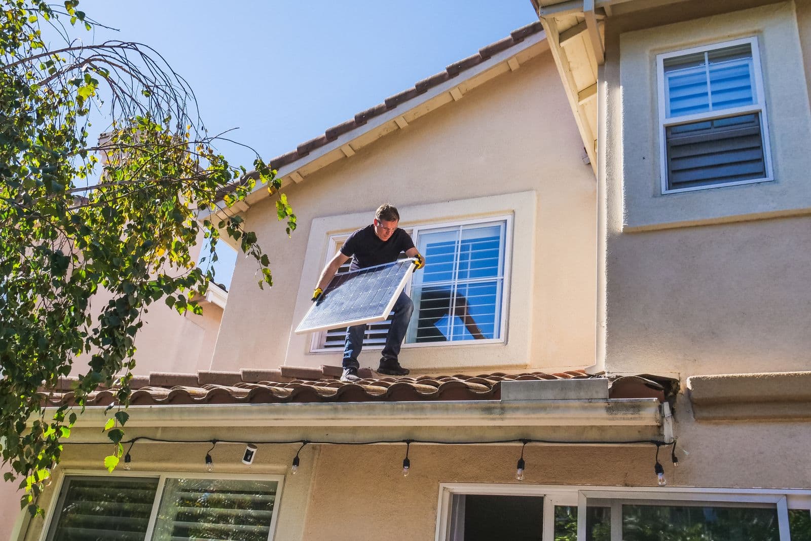 An installer standing on a roof holding a solar panel ready to fit.