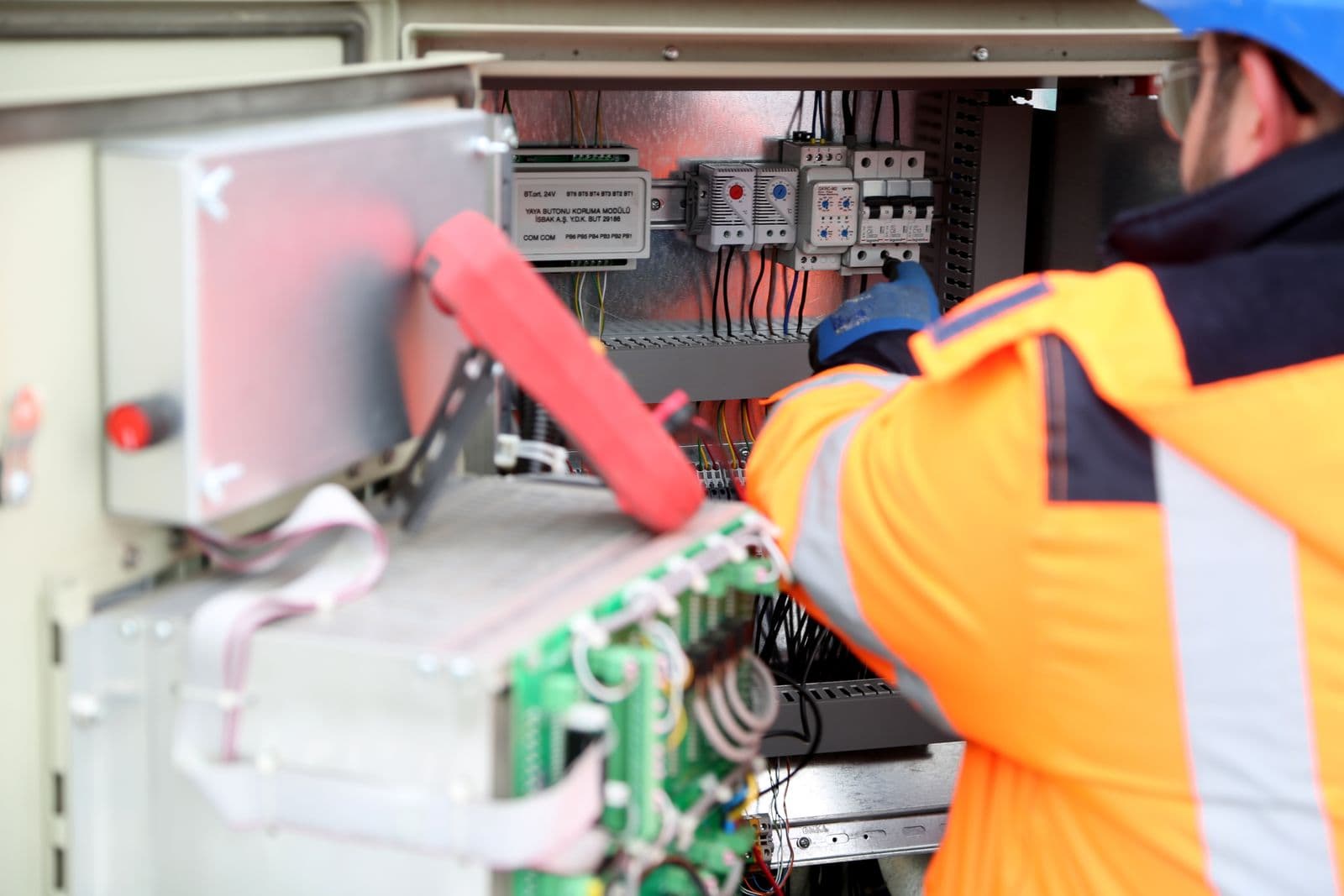 An electrician testing wiring inside an electrical equipment cabinet.