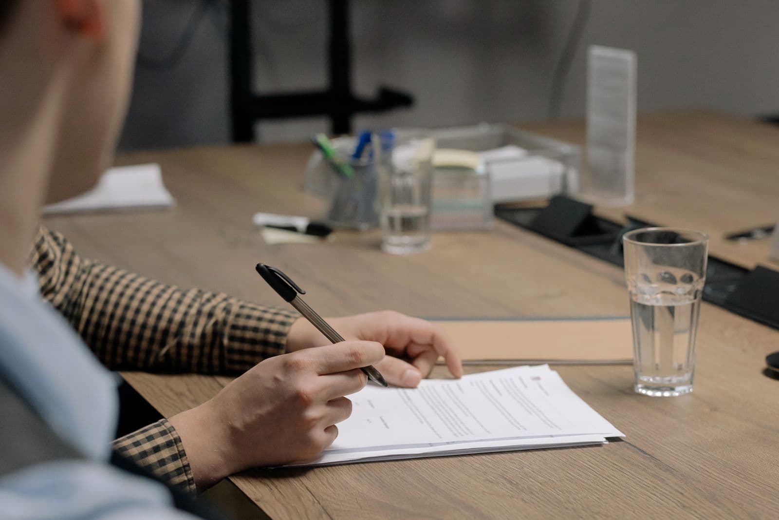 A person signing a document at a wooden table.