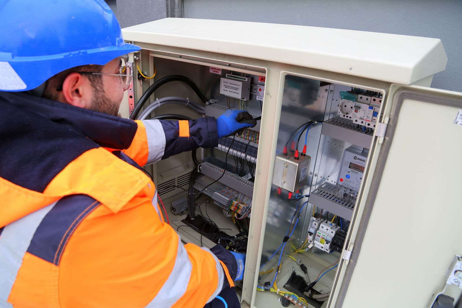 An engineer in safety gear working on an outdoor electrical panel.
