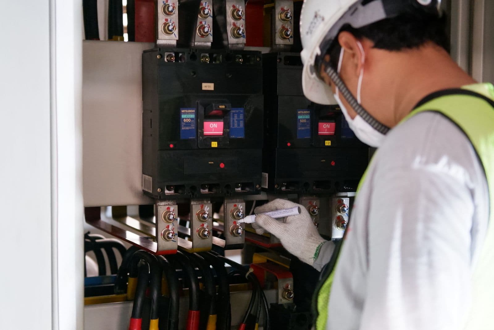 A technician in safety gear checking readings on an electrical panel.