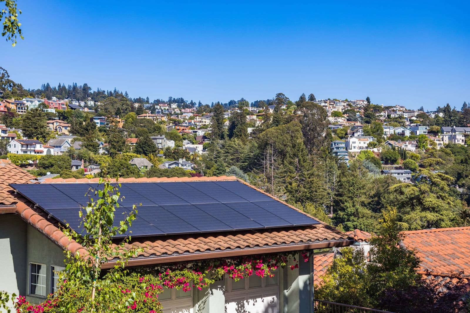 A suburban home with solar panels on the roof, surrounded by greenery.