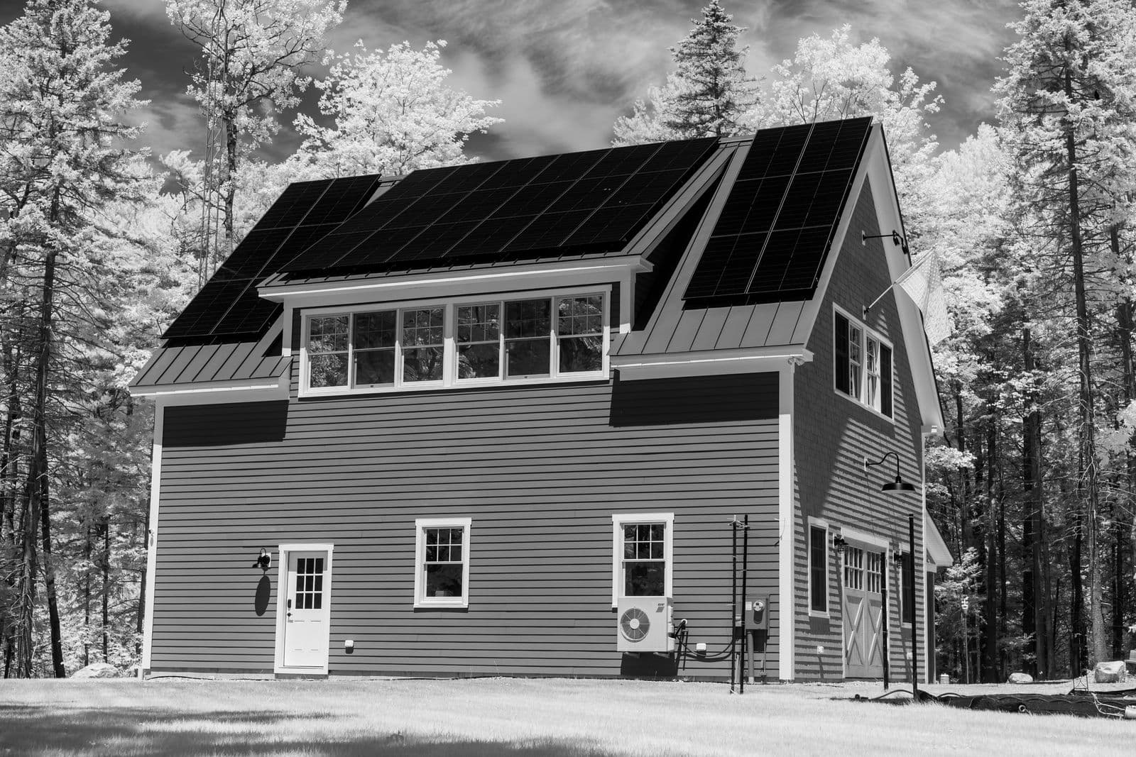 A modern house with rooftop solar panels, surrounded by trees.