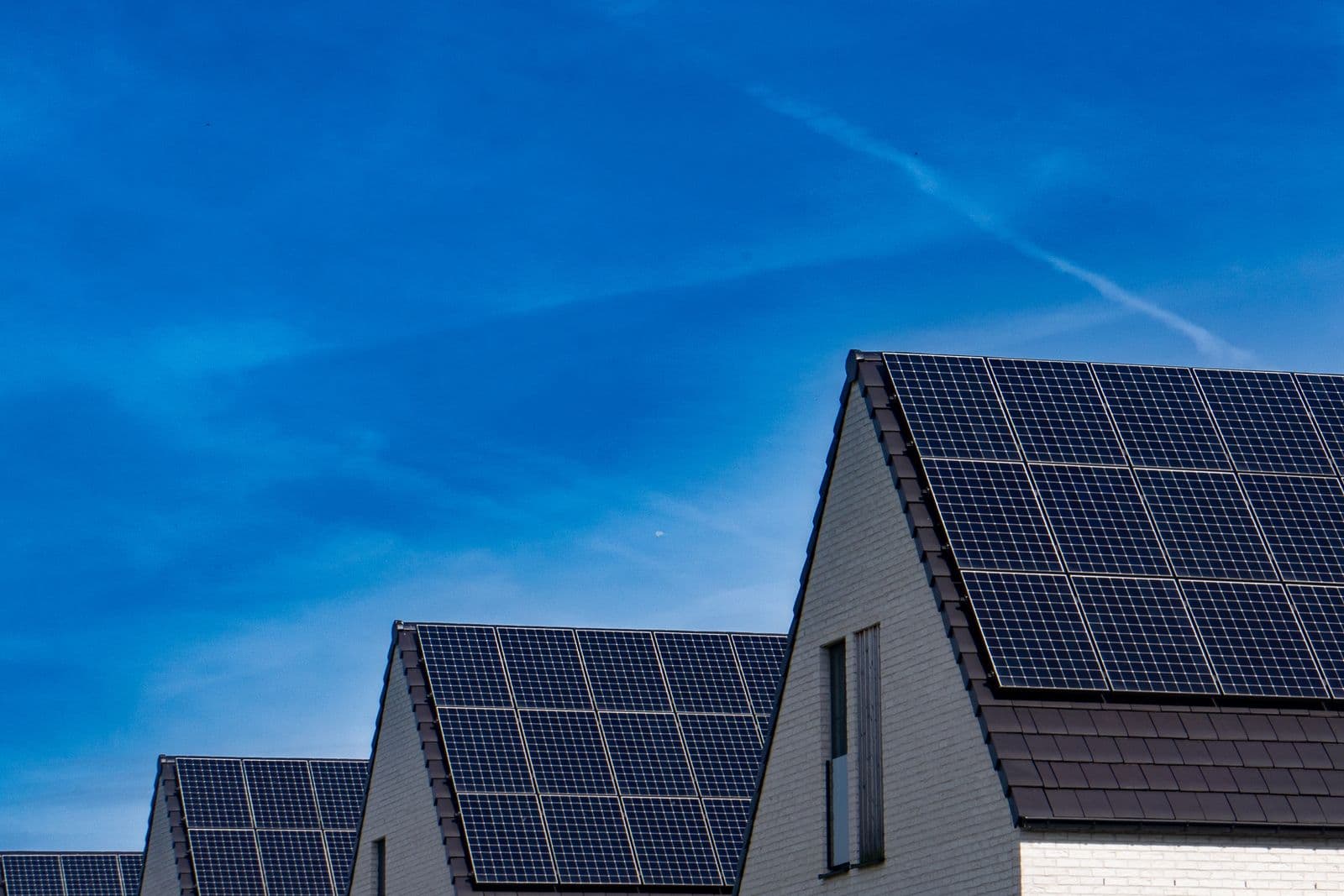 Rows of houses with solar panels on their roofs under a bright sky.